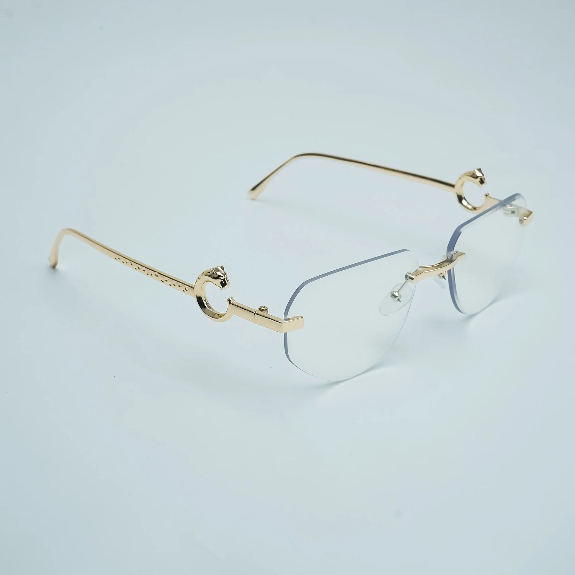Gold rimless eyeglasses with a double bridge and decorative metal details on the temples, shown on a light gray background.